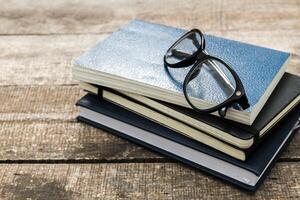 Stacked notebooks with glasses on a wooden surface create an inviting study atmosphere in a cozy setting photo