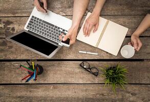 Collaborative work session at a rustic wooden desk with laptop, notebook, and coffee photo