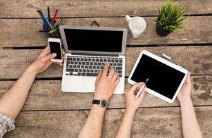 People engaged in technology multitasking at a rustic wooden table during work hours photo