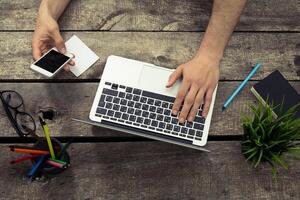 Working on a laptop while using a smartphone in a modern workspace with stationery and plants photo
