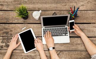 Multiple devices in use during a collaborative work session at a wooden table in a well-lit office environment photo