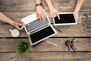 Collaborative workspace on wooden table with digital devices, cups, and stationery during a productive session photo
