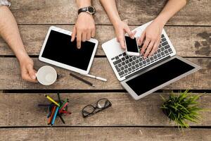 Collaborative workspace with technology and drinks at a wooden table during daytime hours photo