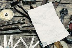 Various vintage tools scattered on a wooden surface with a blank piece of paper ready for notes or sketches photo