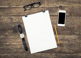 Workspace setup with blank paper, glasses, watch, pencil, and smartphone on rustic wooden table photo