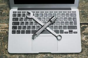 Crossed wrenches placed on a laptop keyboard against a rustic wooden background symbolizing technology and repair photo