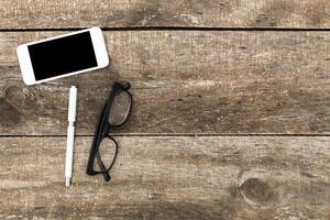 Workspace setup with smartphone, pen, and glasses on wooden table during the afternoon photo