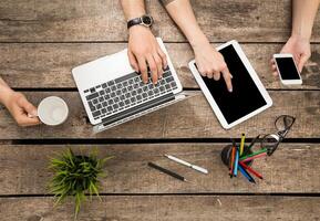 Work collaboration at a rustic table with laptop, tablet, and smartphone during morning hours photo