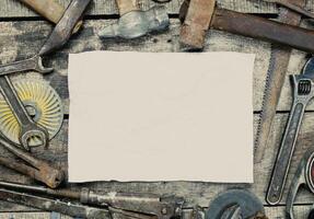 Various hand tools arranged around a blank sheet of paper on a wooden table ready for a project photo