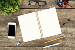 Workspace on a wooden table featuring a blank notebook, smartphone, and stationery items for creative brainstorming photo
