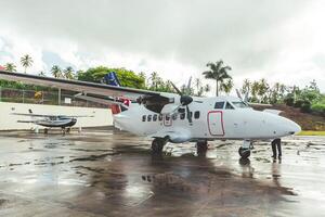 Aircraft parked on a tropical runway with palm trees in the background during an overcast day photo