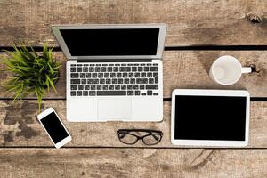 Workspace setup with laptop, tablet, smartphone, and coffee cup on a wooden table during daylight hours photo