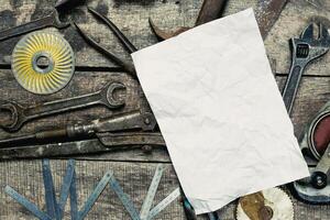 Various hand tools and a blank paper sheet on a rustic wooden surface for crafting or repair projects photo