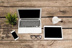 Workspace with laptop, tablet, smartphone, and coffee cup arranged on rustic wooden table during daytime photo