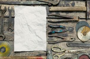 Crafting tools arranged around a blank sheet on a weathered wooden table in a workshop setting photo