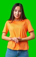 Smiling young woman in orange t-shirt poses with hands together against bright green background photo