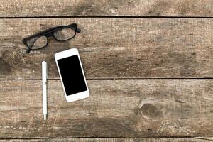 Workspace setup with glasses, smartphone, and pen on rustic wooden table during morning hours photo