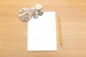 Beach-inspired workspace with seashells, blank paper, and a pencil on a wooden table photo