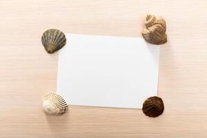 Blank card framed by various seashells on a light wooden surface, perfect for crafting or personal messages photo