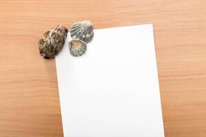 Shells arranged on a wooden surface next to blank paper for creative writing or marine-themed projects photo