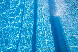 Water ripples in a clear blue swimming pool captured during midday sunlight adding tranquility to the setting photo