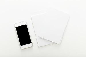 Smartphone and blank sheets resting on a white table, ideal setup for digital note-taking and brainstorming sessions photo