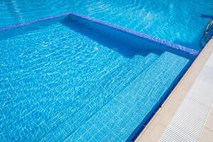Bright blue swimming pool reflecting sunlight, showcasing inviting steps and clear water on a sunny day photo