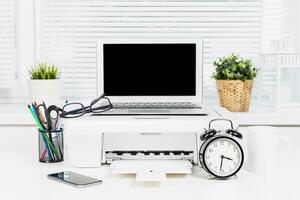 Desk setup with laptop, printer, and office supplies during daytime in a modern workspace photo