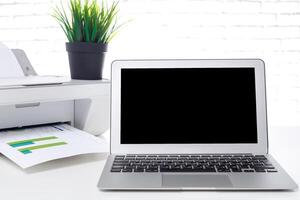 Modern workspace with laptop, printer, and green plant in bright office setting during daylight photo