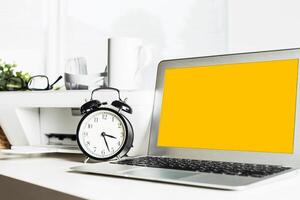 Desk setup with a laptop and clock in a bright office during the morning hours photo