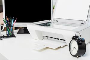 Office workspace featuring a printer, clock, and stationery arranged on a desk with a blank monitor in the background photo
