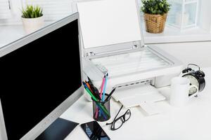 Office workspace features a computer monitor, printer, stationery organizer, coffee cup, and clock against a bright background photo