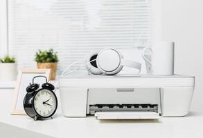 Modern workspace with printer, clock, headphones, and coffee cup captured in a bright office setting photo