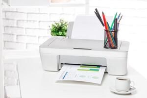 Printer on a desk prints documents while colorful pens stand in a holder near a cup of coffee in a bright workspace photo