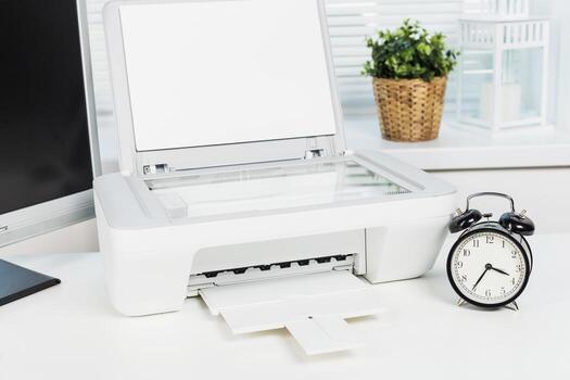 White printer on desk with alarm clock and plant indoors during daytime showing a workspace setting photo