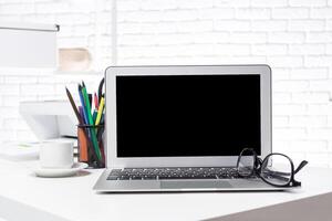 Modern workspace with laptop, glasses, and stationery in a bright office setting photo
