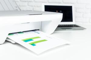 Printer in use producing colorful graphs from a laptop on a modern workspace photo