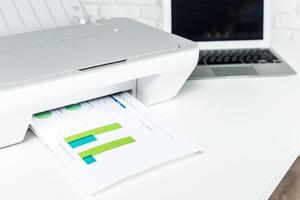 Printer producing document with color graphics beside a laptop on a modern workspace photo