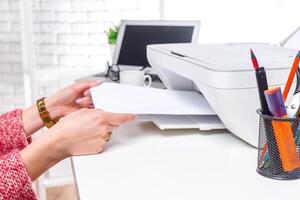 Hands adjusting paper in a printer while surrounded by office supplies in a bright workspace during the afternoon photo