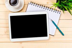 Workspace setup with tablet, coffee, notebook, and plant on wooden table photo