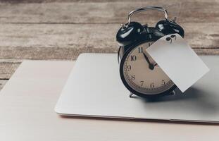 Classic black alarm clock on laptop with price tag resting on wooden table in cozy workspace setting photo