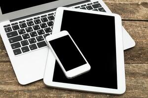 Technology workspace featuring smartphone, tablet, and laptop on wooden table photo