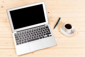 Workspace setup featuring a laptop, a cup of coffee, and a pen on a wooden table in a bright environment photo
