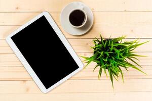 Coffee cup and tablet on a wooden table with a potted plant in a cozy setting during the day photo