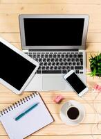 Workspace setup featuring laptop, tablet, smartphone, and coffee cup on wooden desk at early morning photo