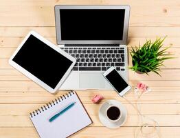 Workspace setup featuring modern gadgets, coffee, and notes on a wooden table during daylight hours photo