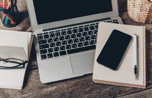 Workspace with a laptop, smartphone, notebook, and stationery on a wooden desk during the daytime photo