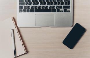Workspace setup with a laptop, notebook, pen, and smartphone on a wooden table photo