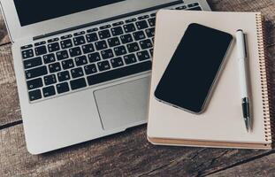 Workspace setup featuring a laptop, smartphone, and notebook on a rustic wooden table photo