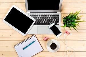 Workspace setup with technology, coffee, and plants on wooden table during daytime photo